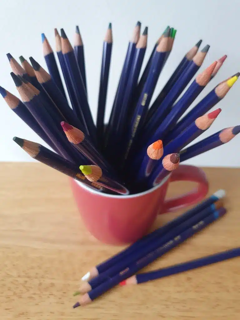 A cup with colored pencils on a wooden surfaces to show