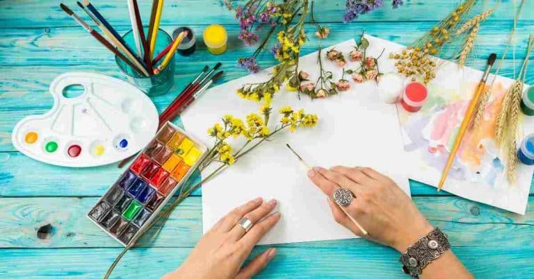 hands holding a paint brush about to start an art journal page to demonstrate art journal prompts