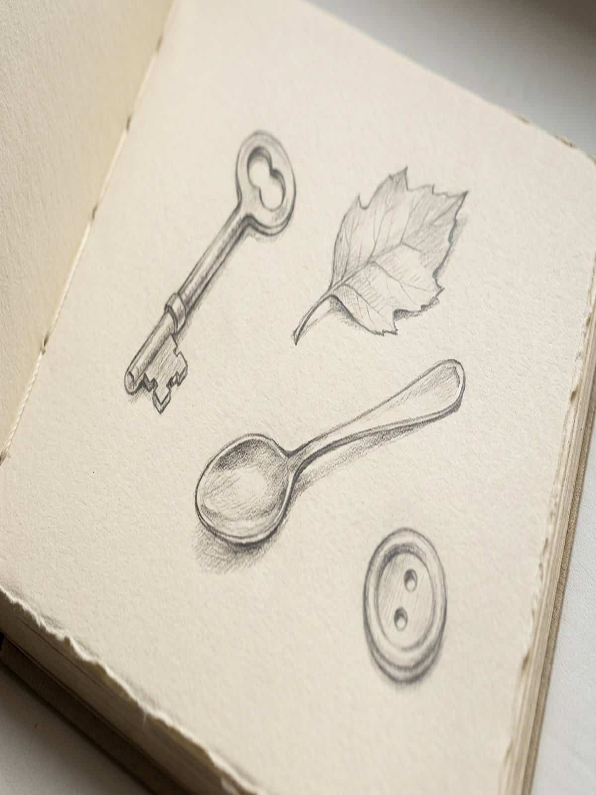 Simple everyday objects sketched in a sketchbook including a key leaf spoon and button