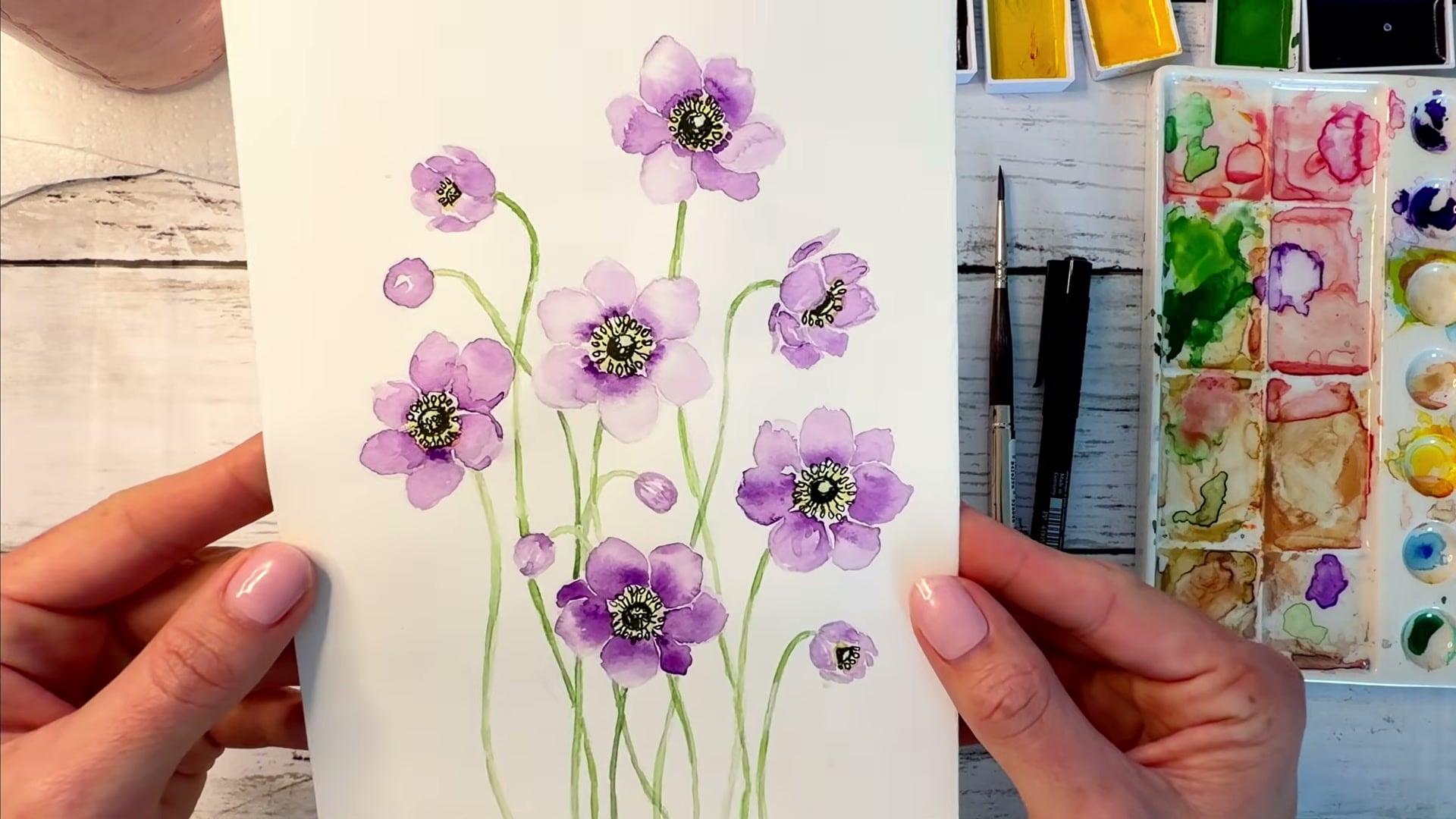 Dee holding up her finished watercolour anemones painting, YouTube tutorial still