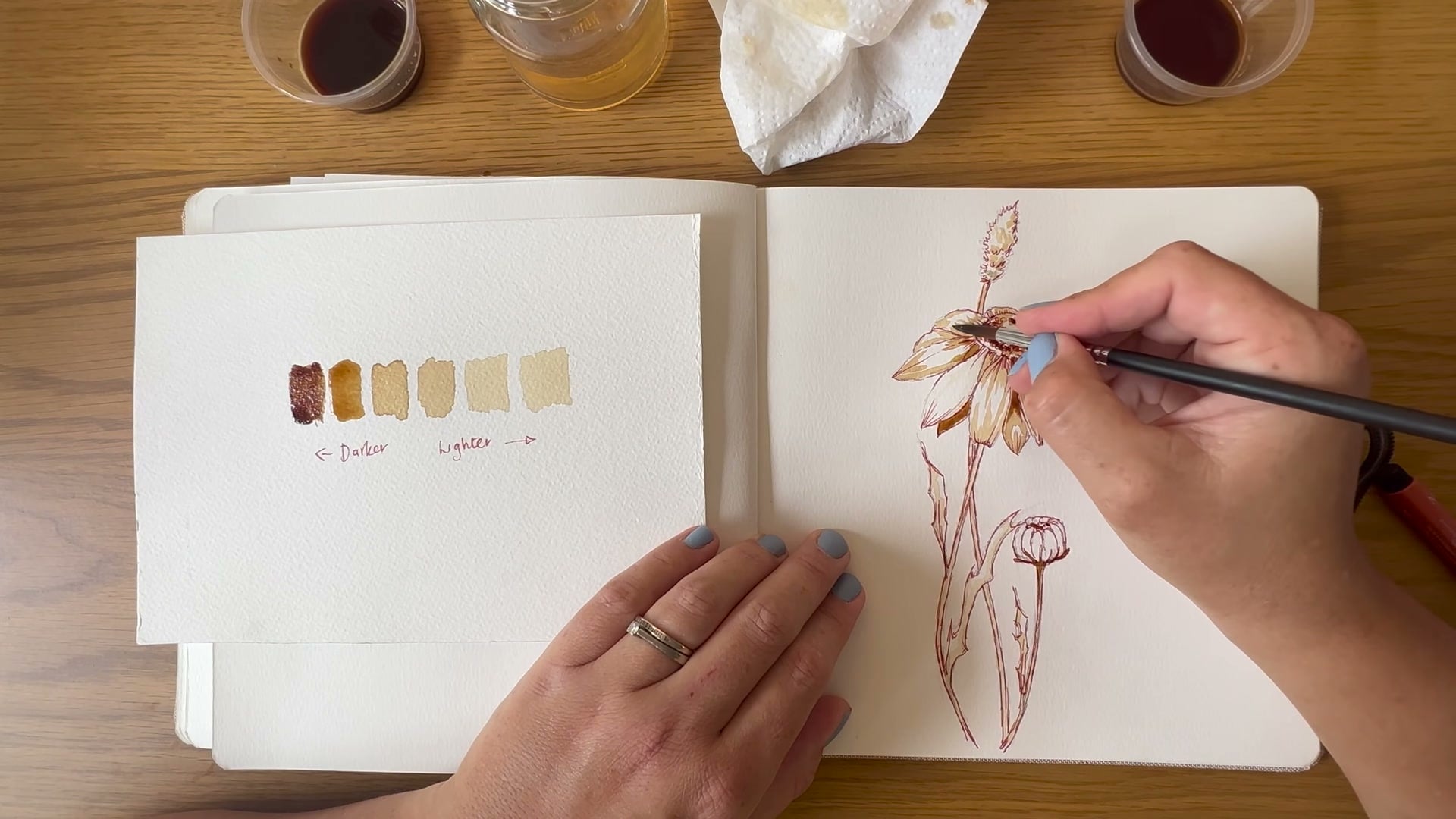 Dee's hands painting a watercolour coffee cup and daisy, YouTube tutorial still