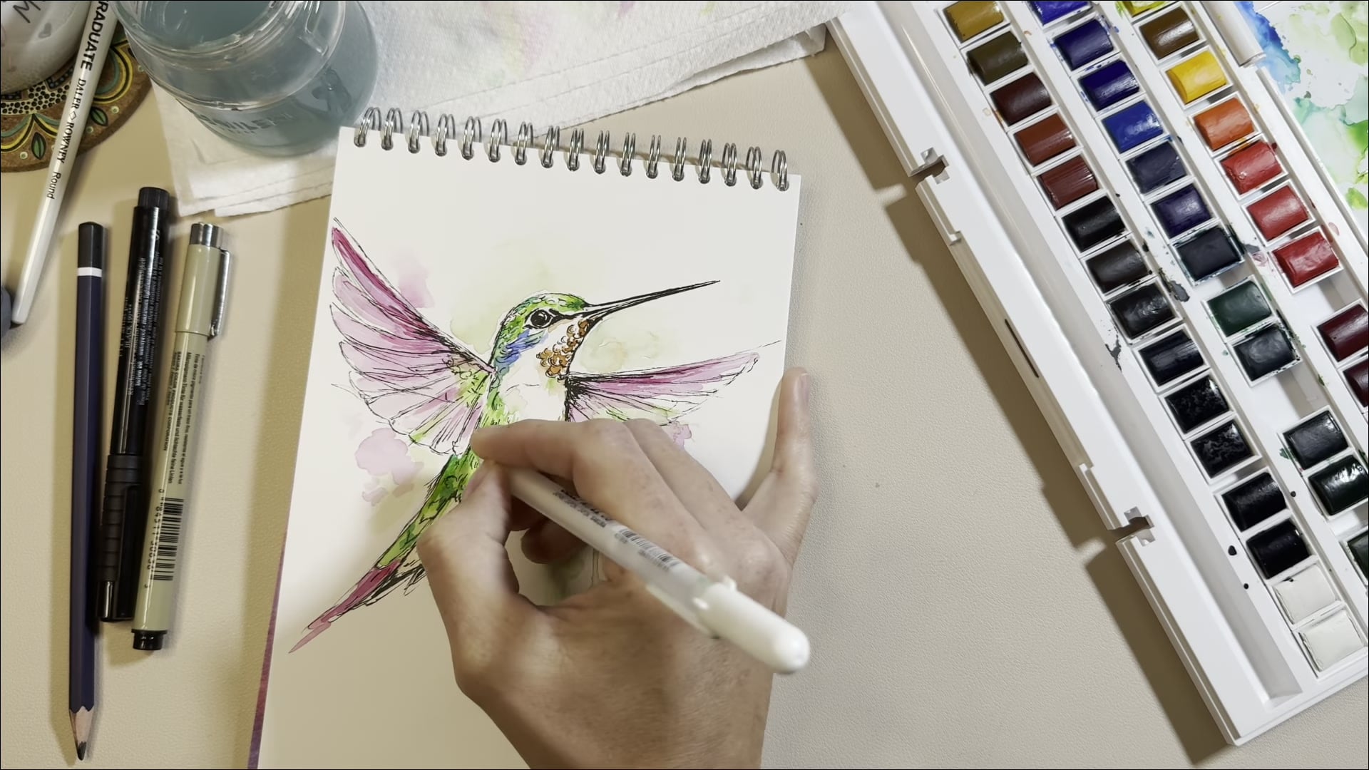 Dee's hands painting a watercolour hummingbird, still from an Artsydee YouTube tutorial
