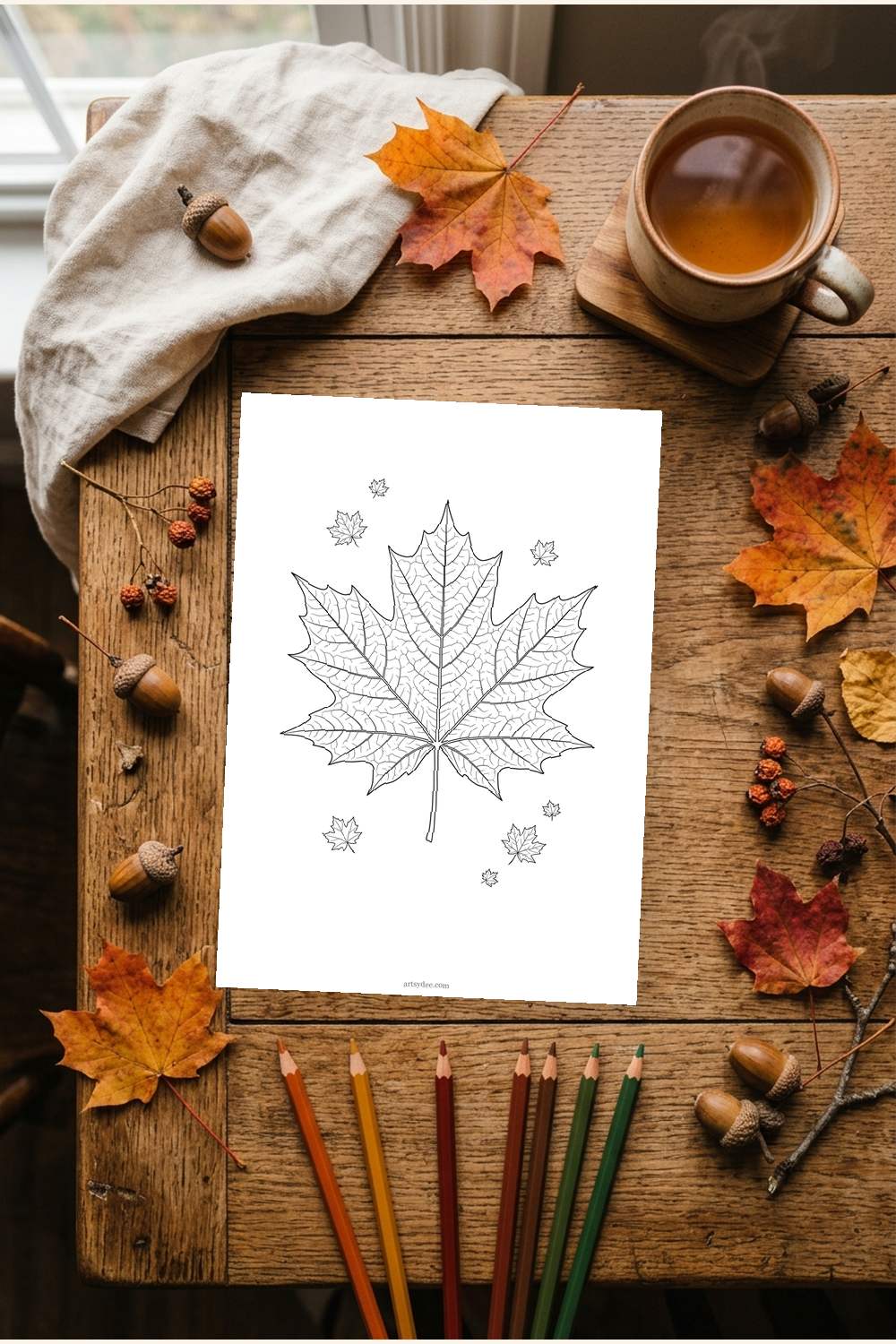 Printed fall leaves coloring page on a desk with colored pencils and a cup of tea