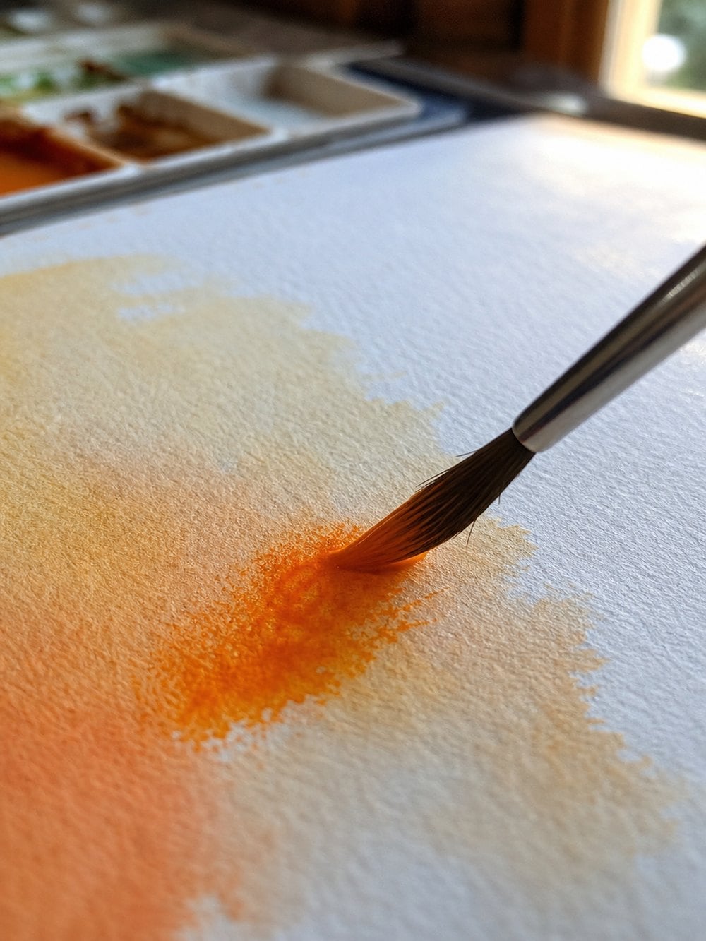 Orange watercolour pigment blooming into a wet sky wash on cold press paper