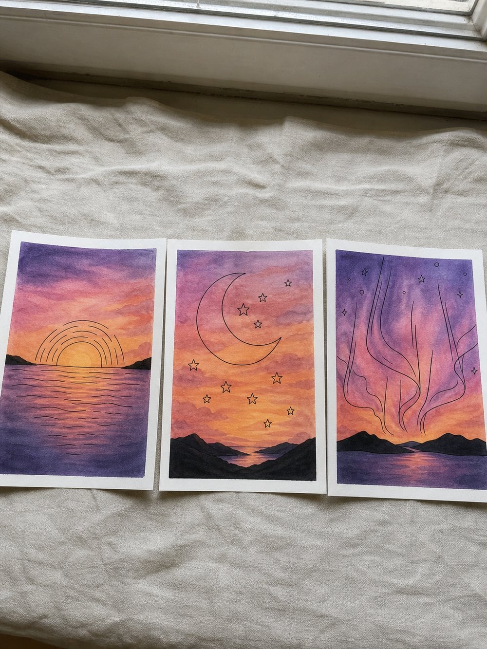 Three finished watercolour sunset paintings drying side by side