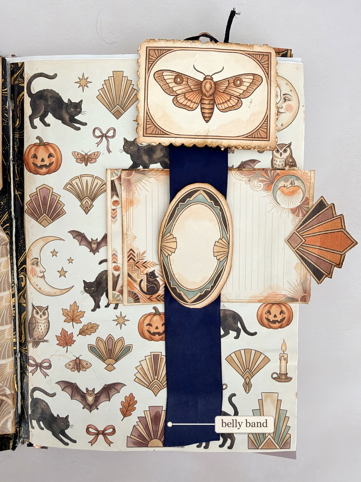 Navy ribbon belly band holding a journaling card on a page, with a moth card on a paper clip at the top