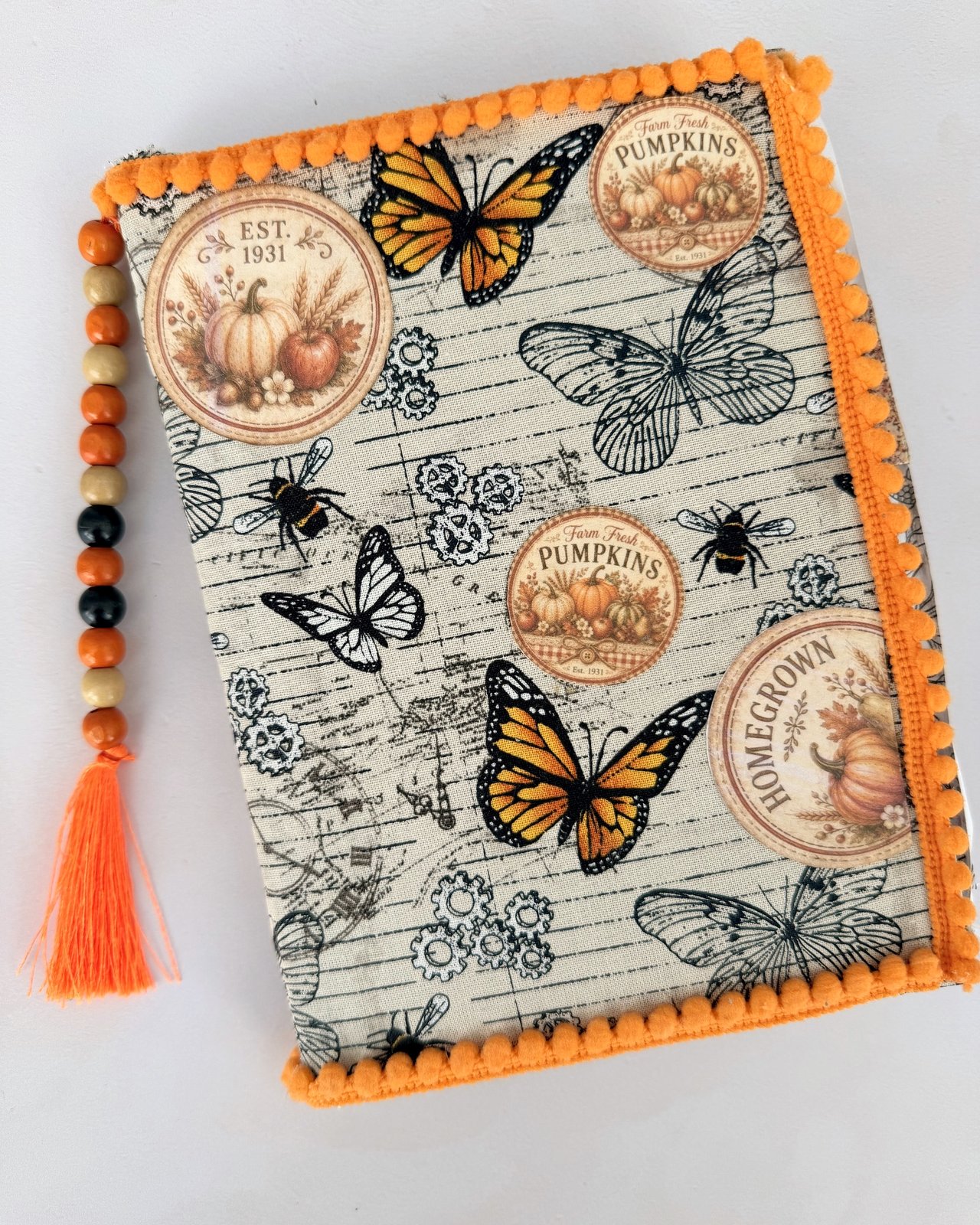 Fabric-covered junk journal with butterfly print, orange pompom trim and a beaded tassel