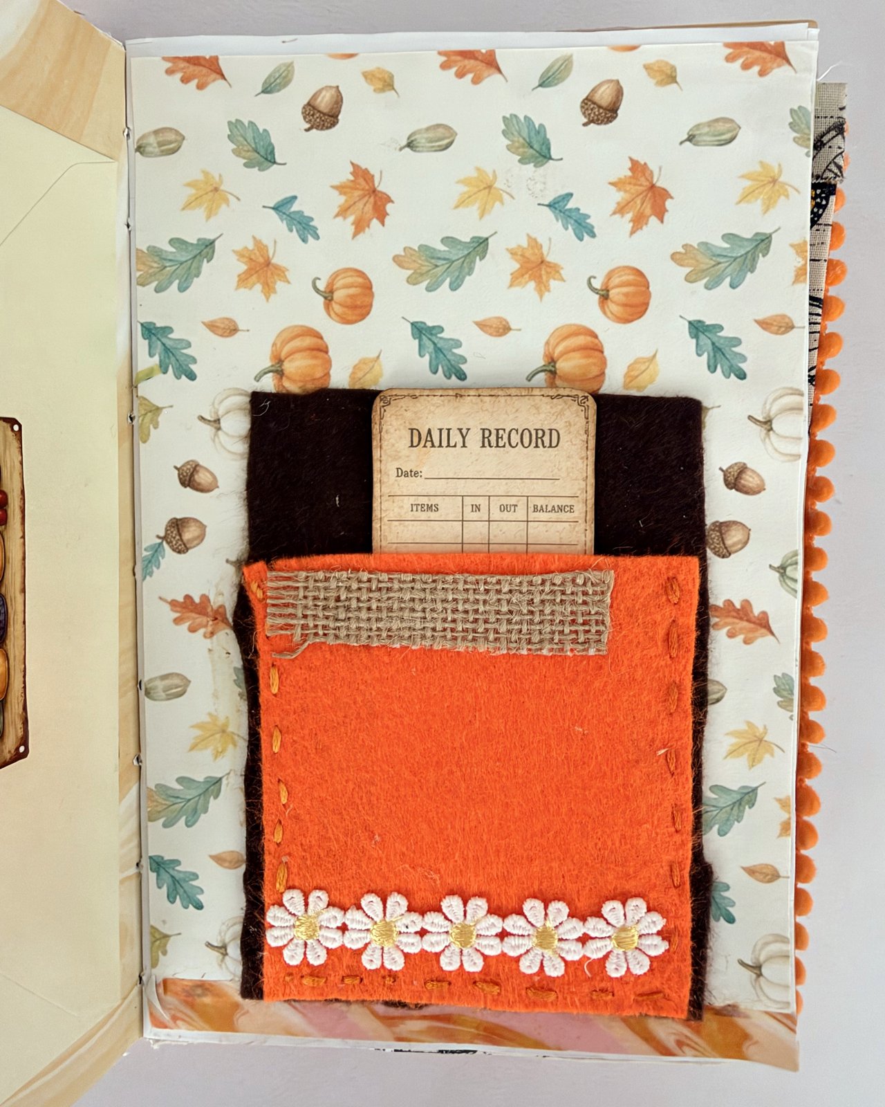 Orange felt pocket with daisy trim and a hessian patch holding a small record card