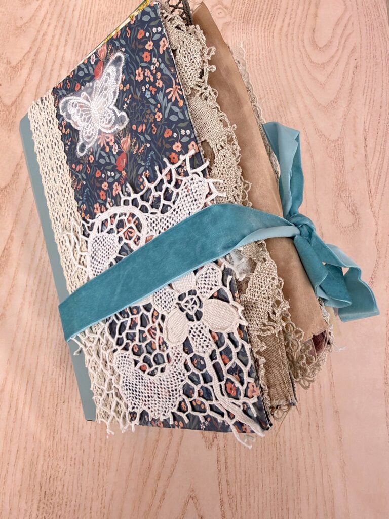 Finished chunky junk journal with a lace-covered front and a blue velvet ribbon tie, made from printable kit pages
