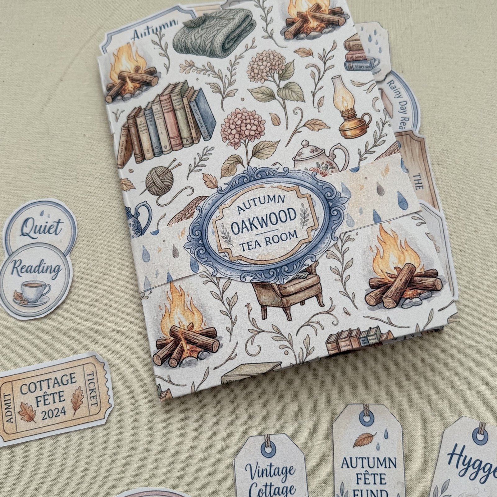 Dee's finished Rainy Cottage journal, its cover printed from the kit and folded, with cut-out tags beside it