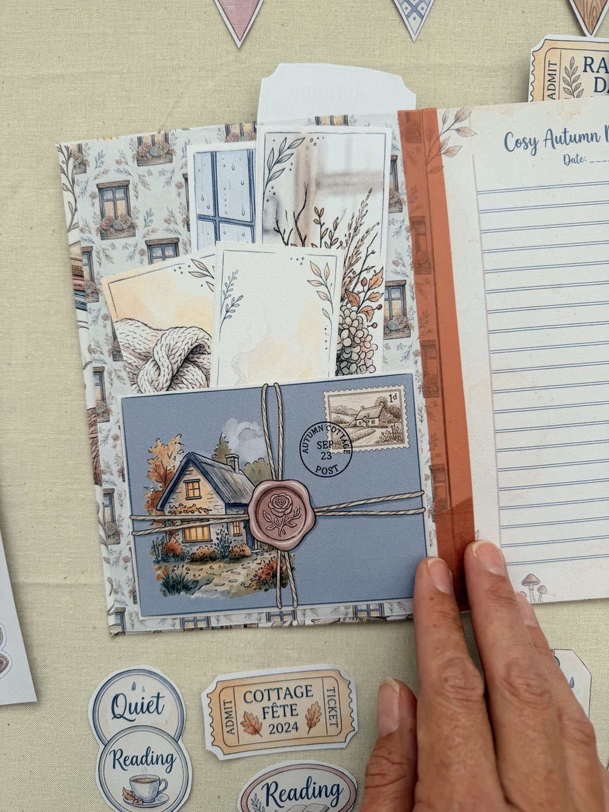 A printed cottage postcard tucked into the front of a page in Dee's Rainy Cottage journal, with a lined insert alongside