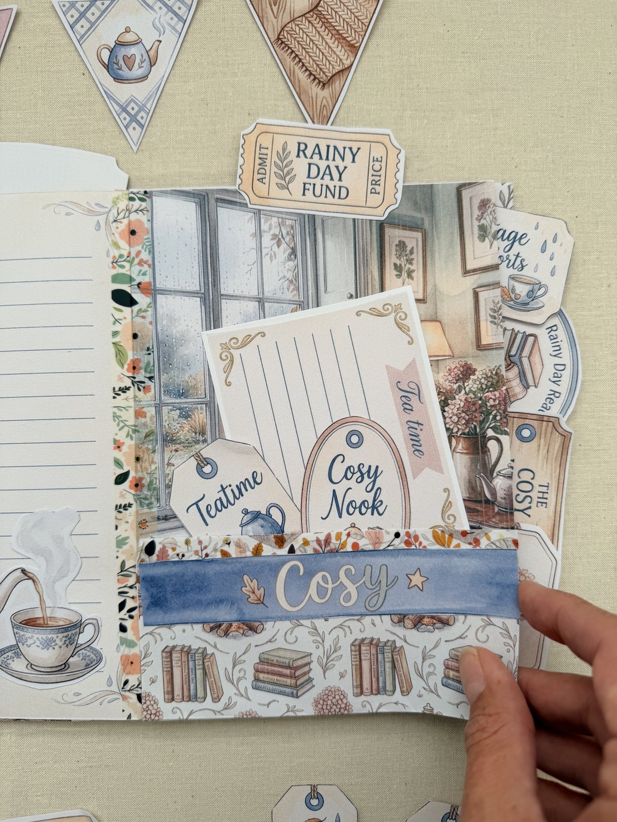 An open spread in Dee's Rainy Cottage journal with printed tags and a ticket tucked along the top edge