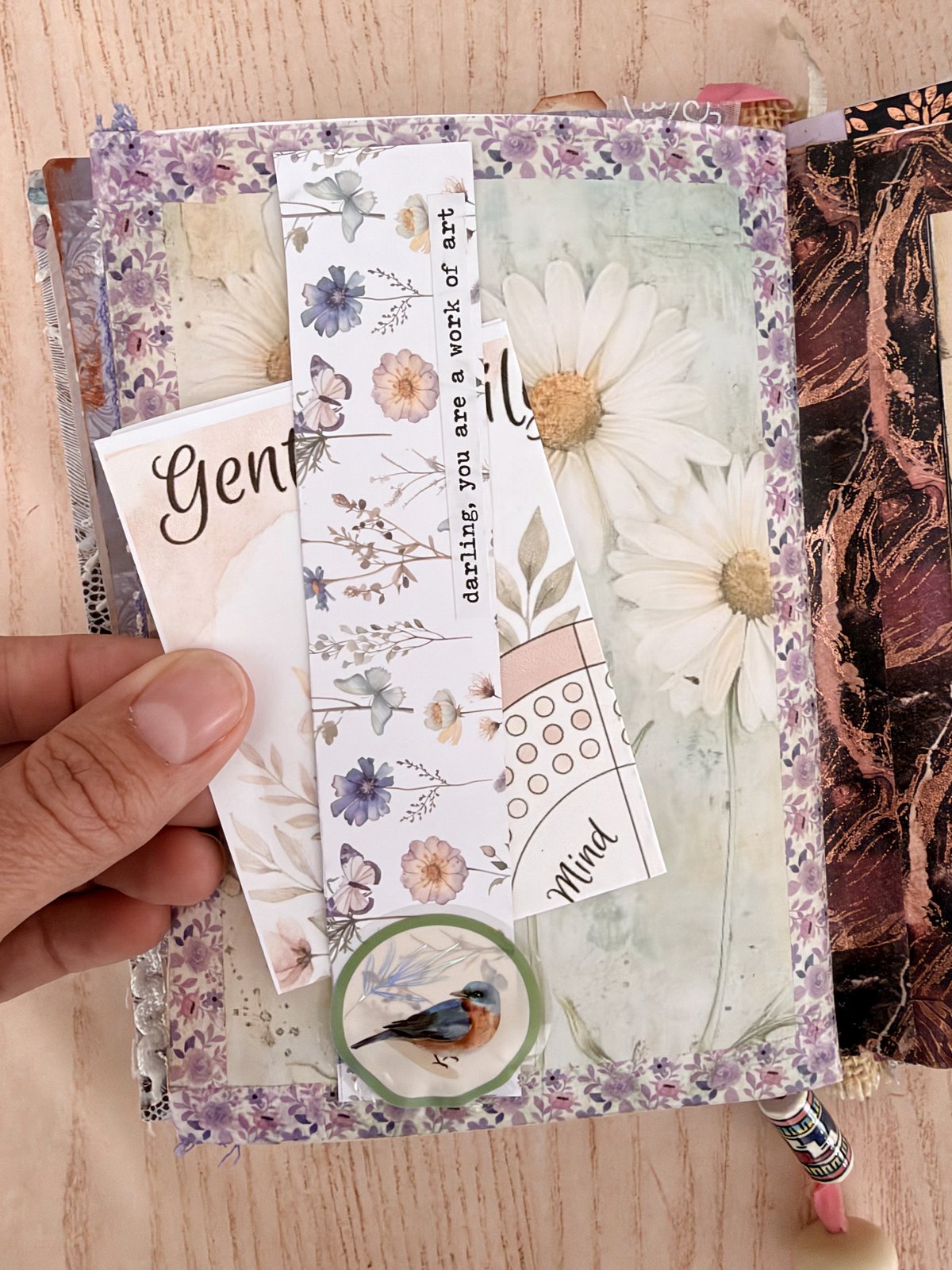Hand holding narrow printable bookmark strips with flowers, a quote and a bird