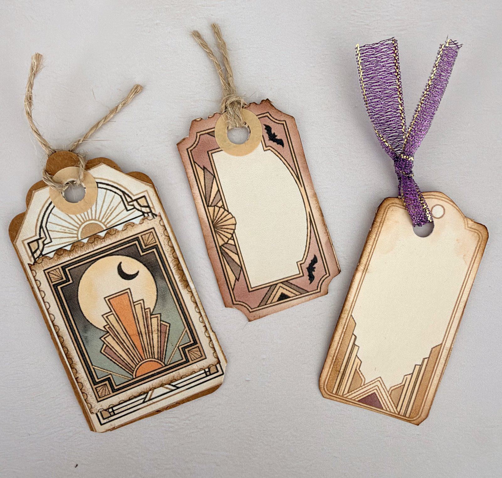 Three handmade junk journal tags cut from printable kit pages, tied with twine and ribbon