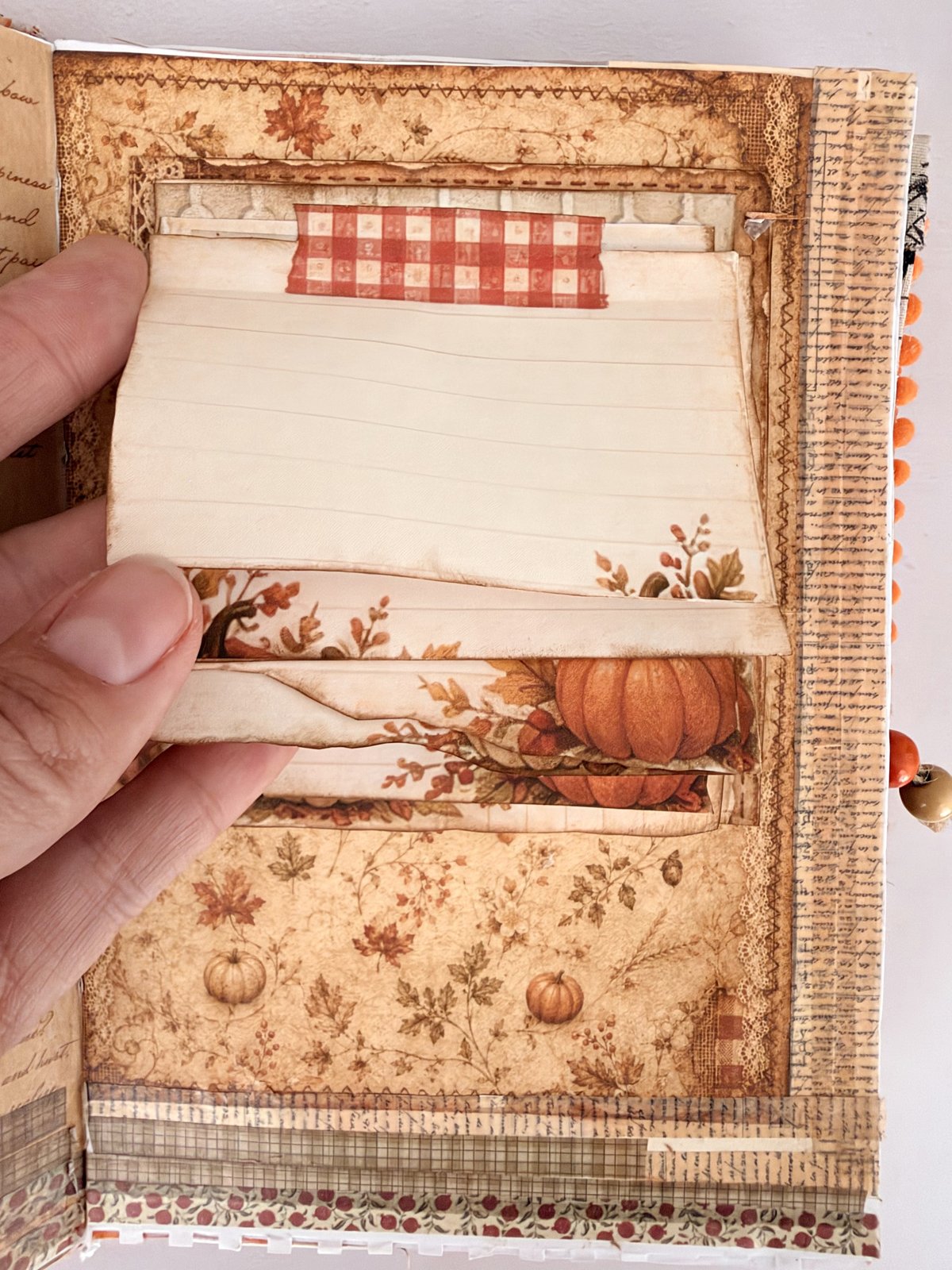 Hand lifting the layered cards of a waterfall notepad topped with gingham washi tape