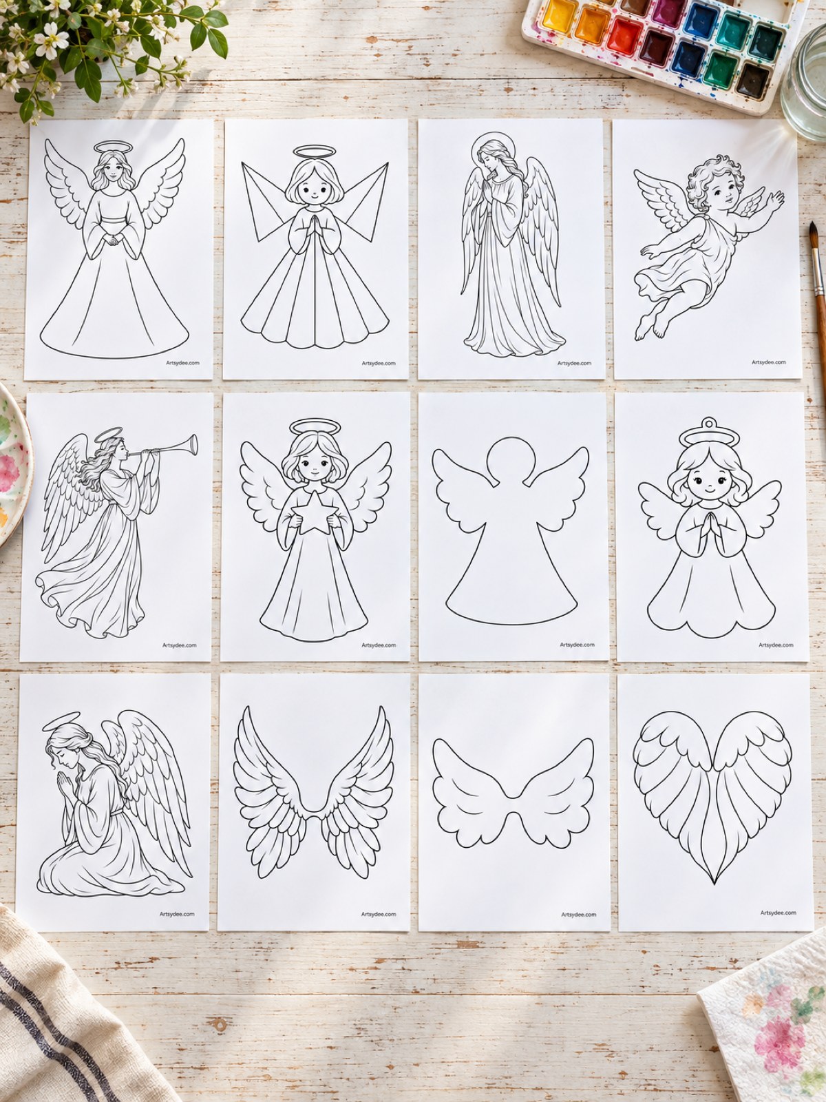 Illustrated mockup of all 12 angel templates printed and spread out on a wooden desk with a paintbrush and a watercolour palette